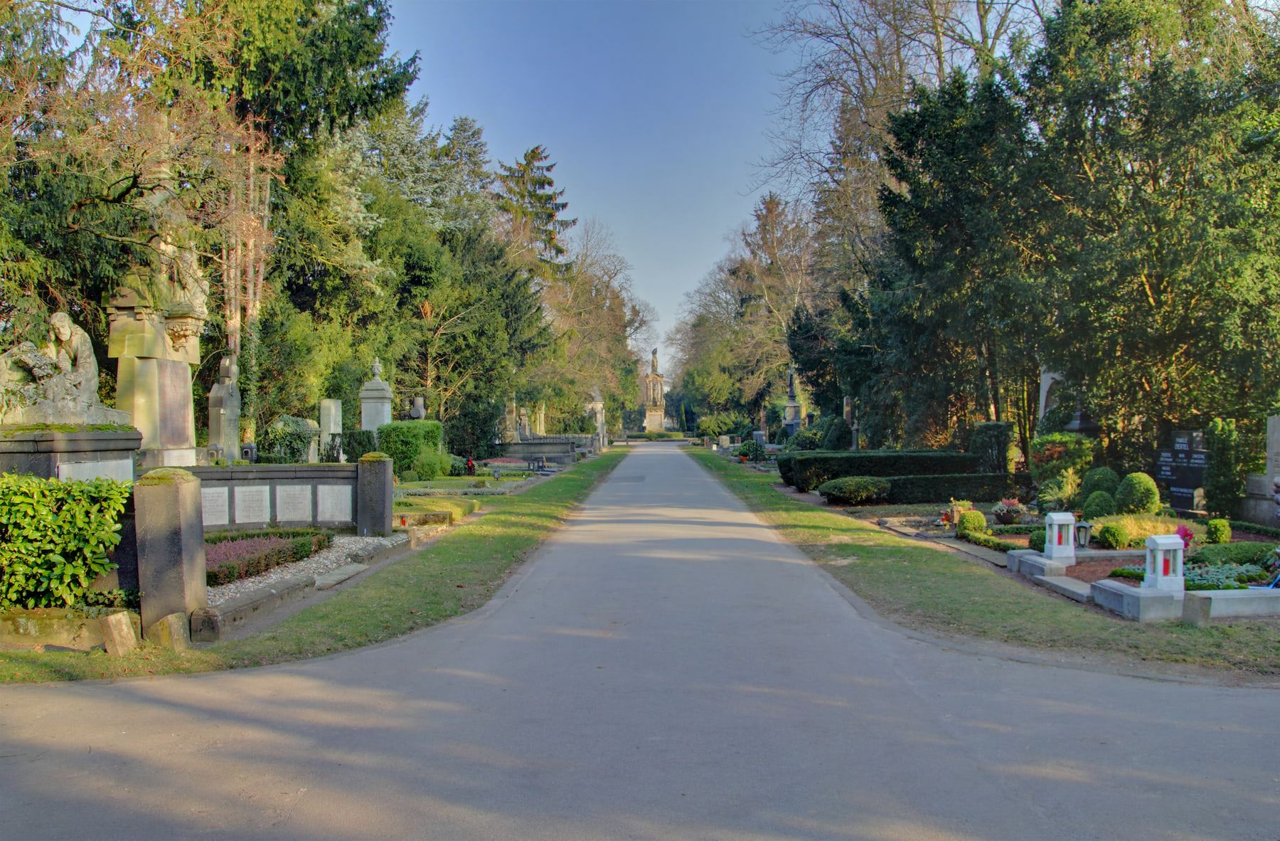 Geradlinige Millionenallee mit monumentalen Grabstätten und geschnittenen Gehölzen zu beiden Seiten auf Melaten-Friedhof